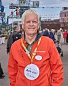 Frivillig med Ask me-skilt fra VisitAarhus står på en havneplads med besøgende i baggrunden.