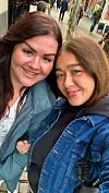 To personer tager en selfie på en brostensbelagt gågade med butikker i baggrunden