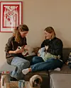 To kvinder sidder på en sofa med et barn i en hyggelig stue