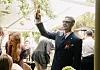 Mand i jakkesæt holder en ølflaske højt under en travl udendørs reception.