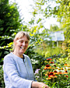 Kvinde i lys trøje passer blomster i en grøn og solrig have