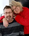 Midaldrende par sidder tæt sammen i en lys stue og smiler mod kameraet