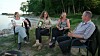 Fire personer sidder i stole og taler sammen ved en kyst med skov bagved.