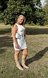 Kvinde i lys kjole står på græs foran et træ i solskin