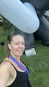 Kvinde med medalje tager selfie foran oppustelig struktur og 50 km-skilt på græsplæne.