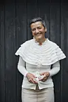 Smilende kvinde i lys bluse står foran en mørk trævæg