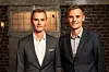 To mænd i jakkesæt står foran en murstensvæg i et studie