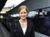 Kvinde med taske står på togperron foran et moderne tog
