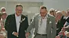 Brudepar i jakkesæt går hånd i hånd gennem ris kastet af smilende gæster.