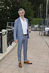Mand i blåternet jakkesæt står med et glas på en terrasse med dækkede borde.