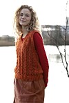 Kvinde i orange strikvest står udendørs foran vand og sløret baggrund.