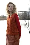 Kvinde i orange strikvest står udendørs foran vand og sløret baggrund.