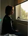 Kvinde sidder på seng og kigger ud ad et vindue i varmt aftenslys
