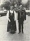En kvinne og en mann i tradisjonelle klær står ute på en plass med biler i bakgrunnen.