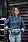 Kvinde i blå mønsterstrikket sweater står foran en mørk trævæg.