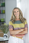 Kirstine Virén står i et lyst rum med farverig bluse og blomster i baggrunden.