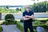 Lars Bom står i Aagerup Kirkes have med grønt anlæg og udsigt til søen bagved.