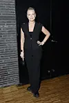 Person i sort buksedragt poserer foran sort dør på trægulv ved Strax-arrangement.