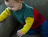 Baby i flerfarvet striktrøje sidder og støtter sig til en grøn sofa