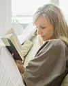 Kvinde sidder i sofa og læser en bog ved et lyst vindue.