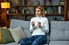 Kvinde på sofa holder en graviditetstest med én streg og ser berørt ud.