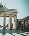 Brandenburger Tor i solskin med gående mennesker og lange skygger på pladsen