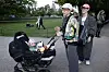 To voksne går med barnevogn på grussti i grøn park