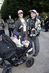 To personer står med en barnevogn fyldt med legetøj på en parksti omgivet af mennesker.