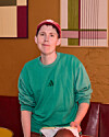 Person i grøn Adidas-sweatshirt og rød kasket i farverigt caféinteriør.
