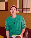 Person i grøn Adidas-sweatshirt og rød kasket i farverigt caféinteriør.