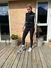 Kvinde på træterrasse med medicinsk fodstøvle foran murstenshus.