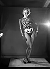 Kvinde i skeletkostume står på et lille podium i et oplyst fotostudie, 1959