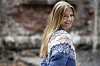 Person i blå mønstret striktrøje smiler foran en sløret murstensbaggrund.