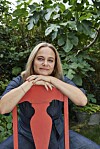 Maren Uthaug hviler armene på ryglænet af en rød stol i en grøn have