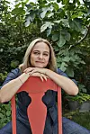 Maren Uthaug hviler armene på ryglænet af en rød stol i en grøn have