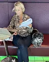 Kvinde sidder på bænk med bærbar computer og hund ved siden af