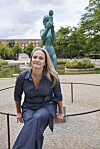 Maren Uthaug sidder foran springvand og bronzeskulptur i grøn bypark