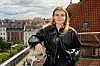Una Plesner står på tagterrasse med udsigt over røde tage og bybygninger.