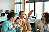 Tre forretningskvinder giver hinanden highfives i et lyst, åbent kontor.