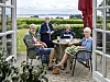 Fire seniorer sidder ved havebord på terrasse i Rønde med udsigt til fjord og marker.