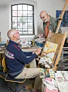 To ældre beboere maler sammen ved et staffeli i et lyst atelier i Rønde