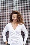 Julia Lahme i hvid bluse står foran en grå perforeret metalvæg