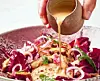 Hånd hælder cremet sauce over farverig kyllingeret i en dyb tallerken.