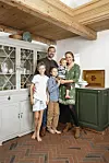 Familie står samlet foran vitrineskab og grøn køkkenbænk i hyggeligt landkøkken.
