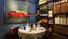 Rundt dækket bord i restaurant omgivet af vinflasker, træreoler og stort billede af kød