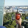 Hånd holder rød cocktail med udsigt over havn og by i baggrunden