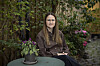 Trine Hjorth Bønnerup sidder ved et lille bord i en gårdhave omgivet af grønne planter.