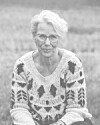 Ældre kvinde med briller i mønstret sweater sidder udendørs.