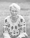 Ældre kvinde med briller i mønstret sweater sidder udendørs.