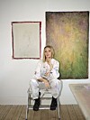 Nikoline Liv Andersen sidder på en stige foran to abstrakte billeder i sit atelier.